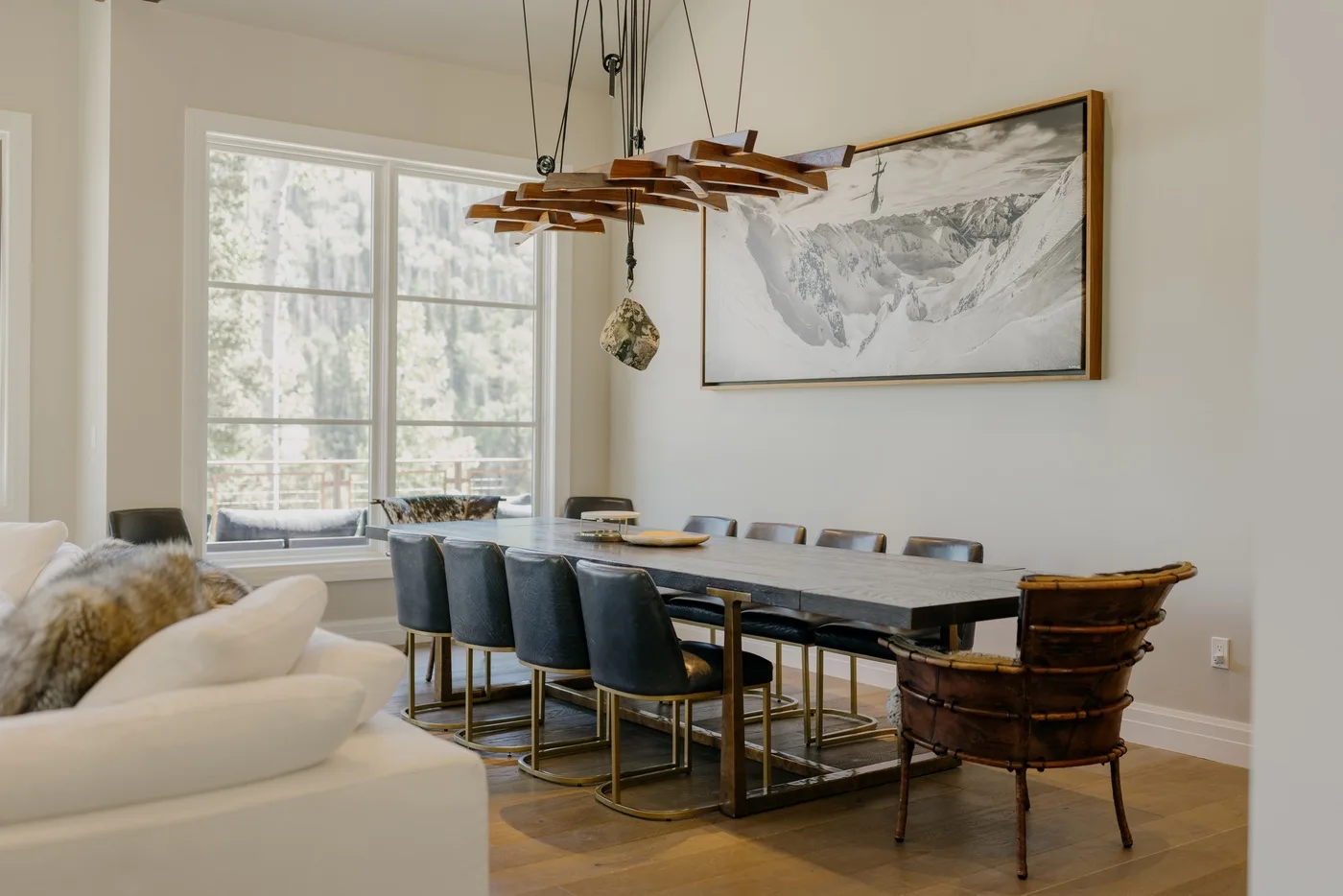 A dining area with a long table and upholstered seating beside a large window.