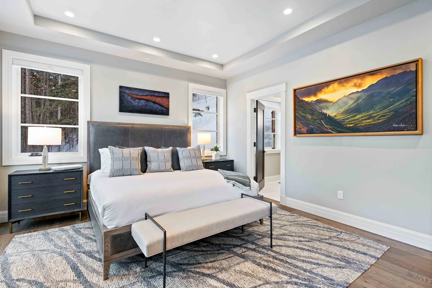 A bedroom with a large bed, bedside tables, and framed landscape art.
