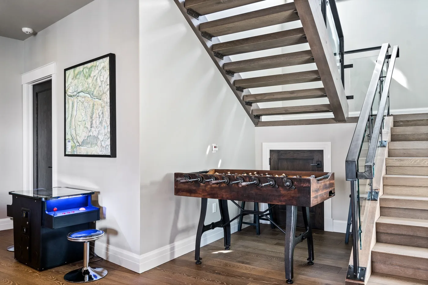 A foosball table sits beneath an open staircase in a bright interior.