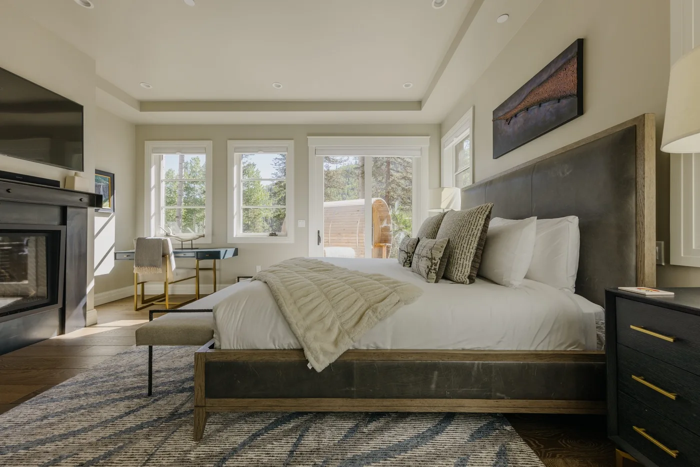 A bright bedroom features a large bed, windows, and a fireplace.