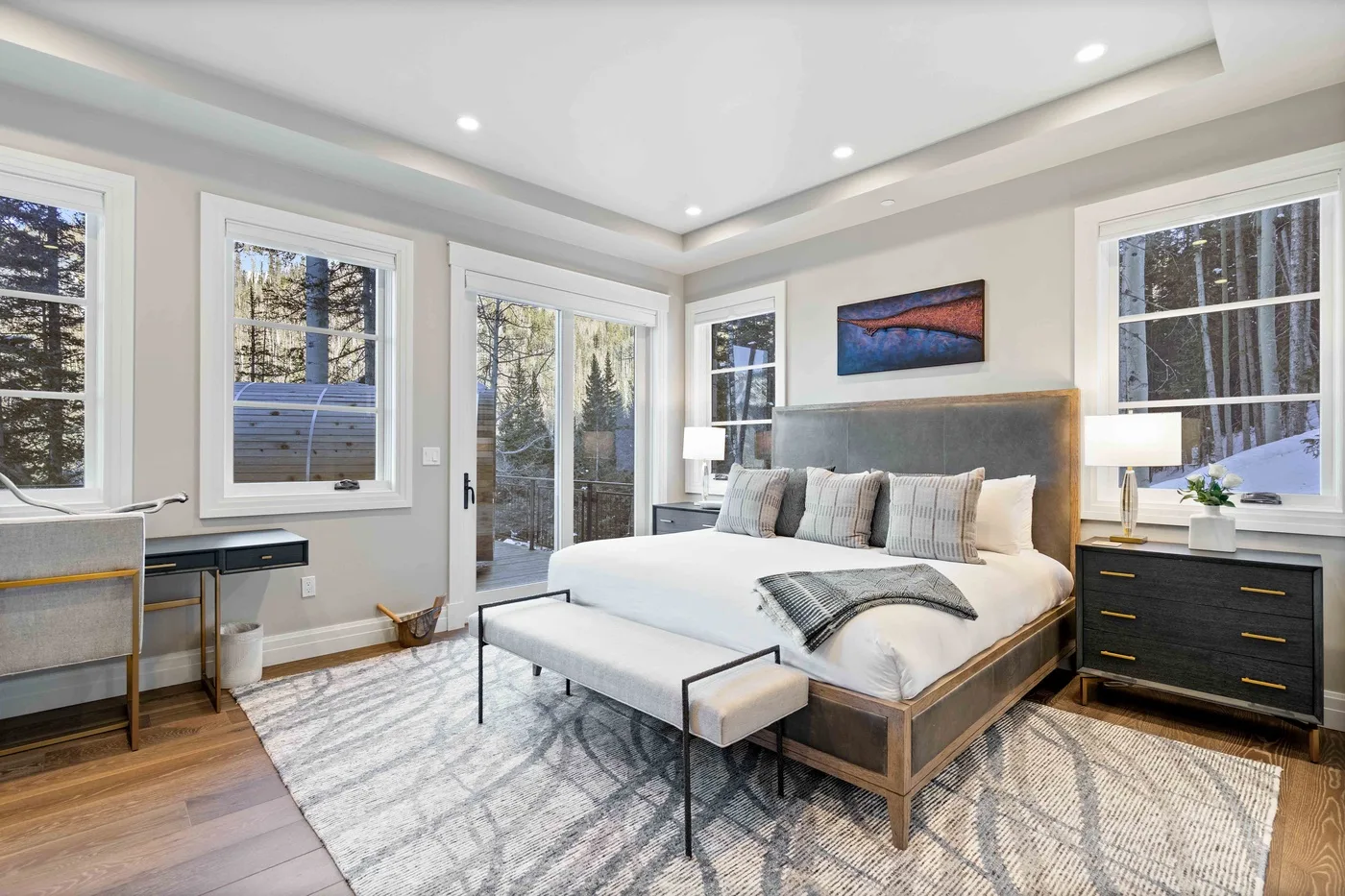 A bright bedroom with a large bed, a rug, and several windows.
