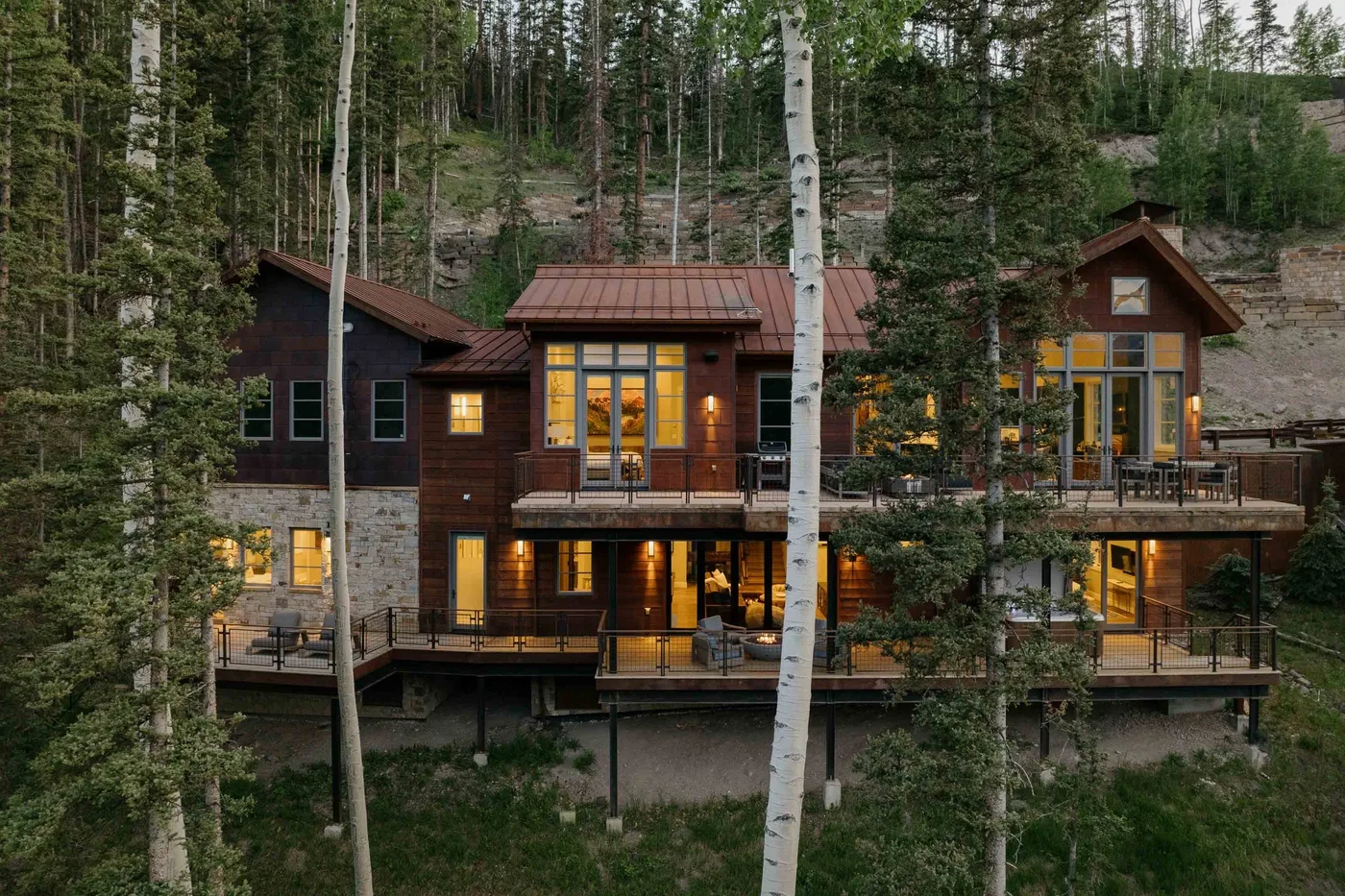 A multi-level cabin nestled among trees, with warm lights glowing through its windows.