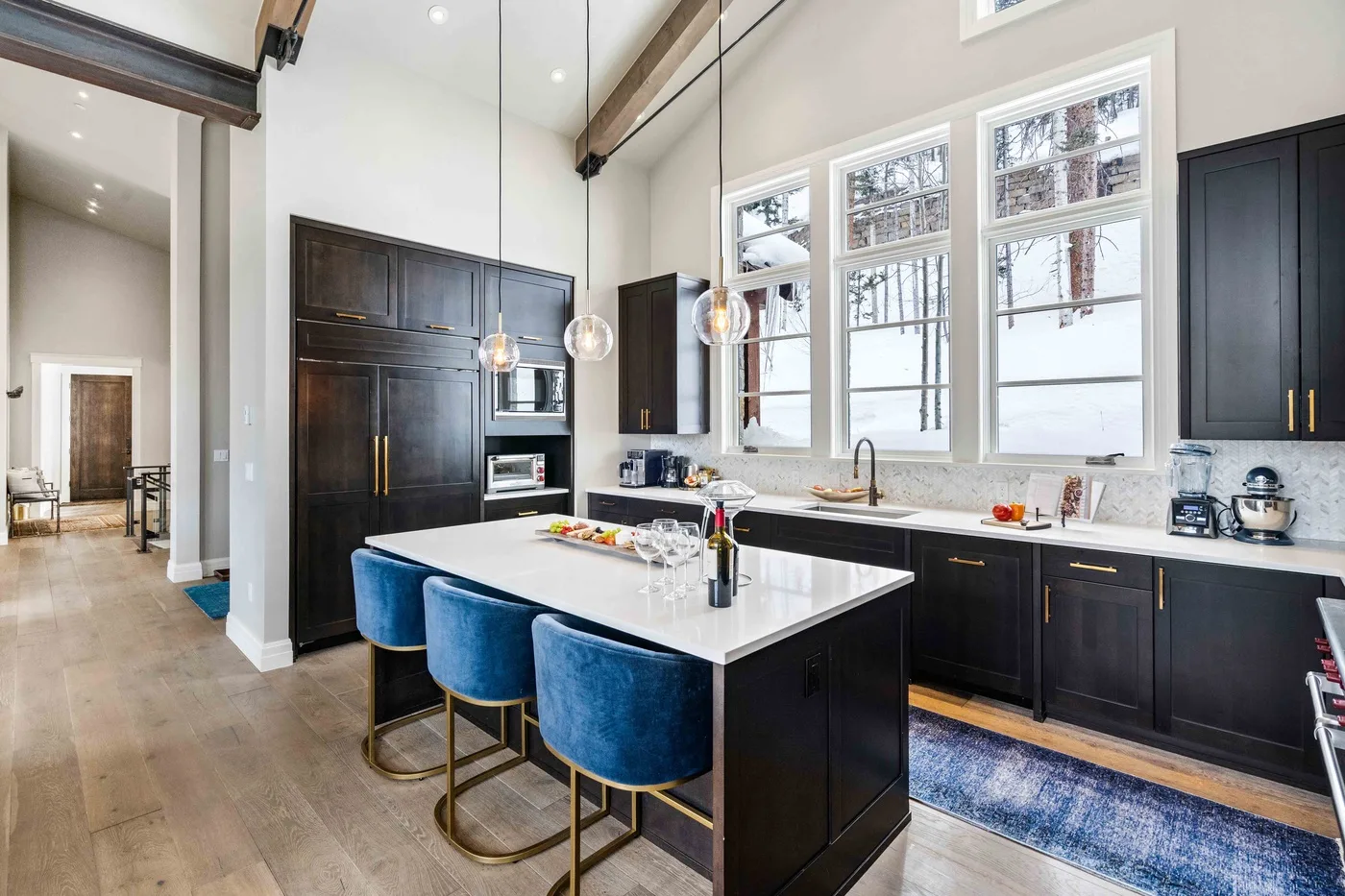 A bright kitchen with a large island, dark cabinets, and blue seating.