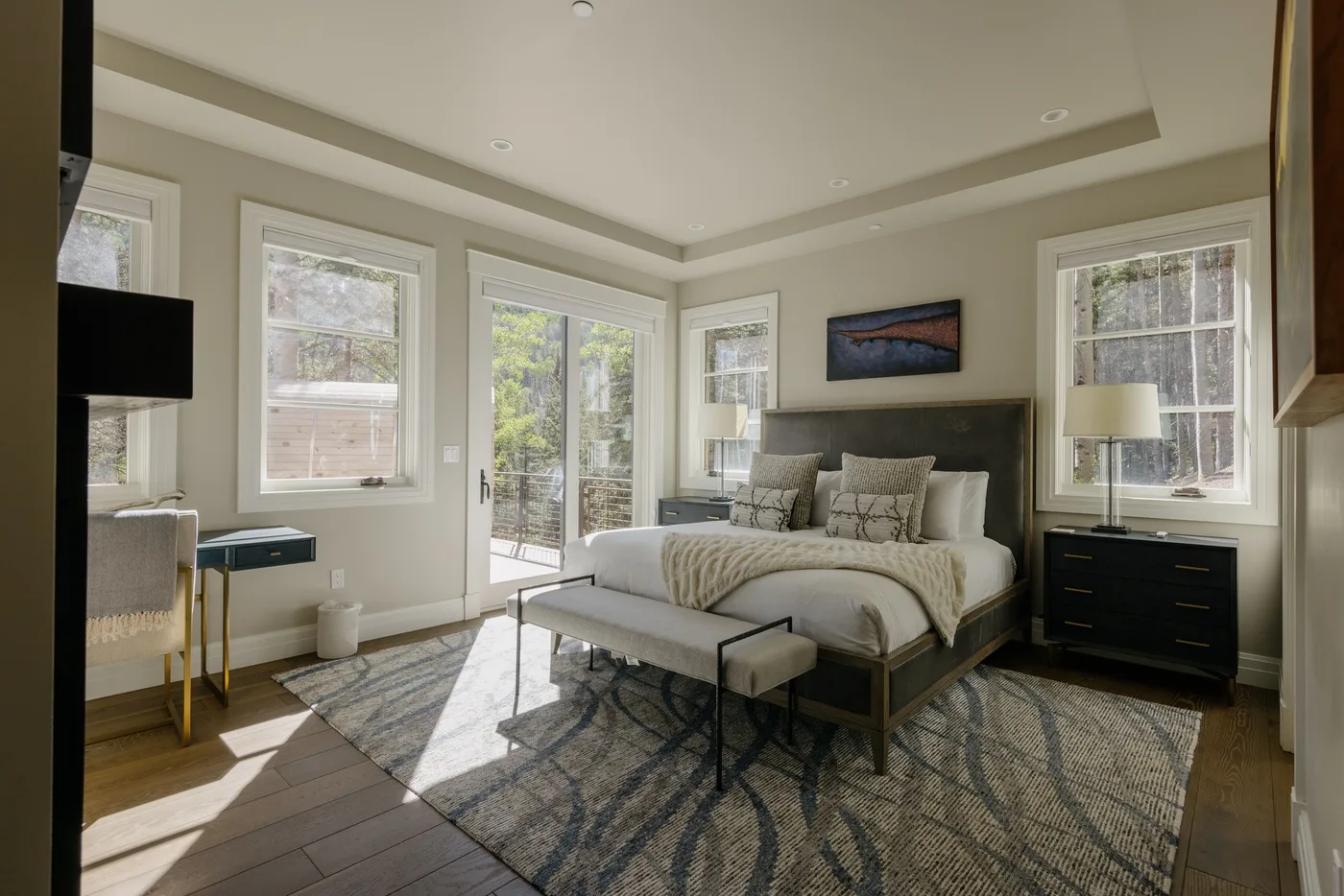 A bright bedroom with a bed, large windows, and a patterned rug.