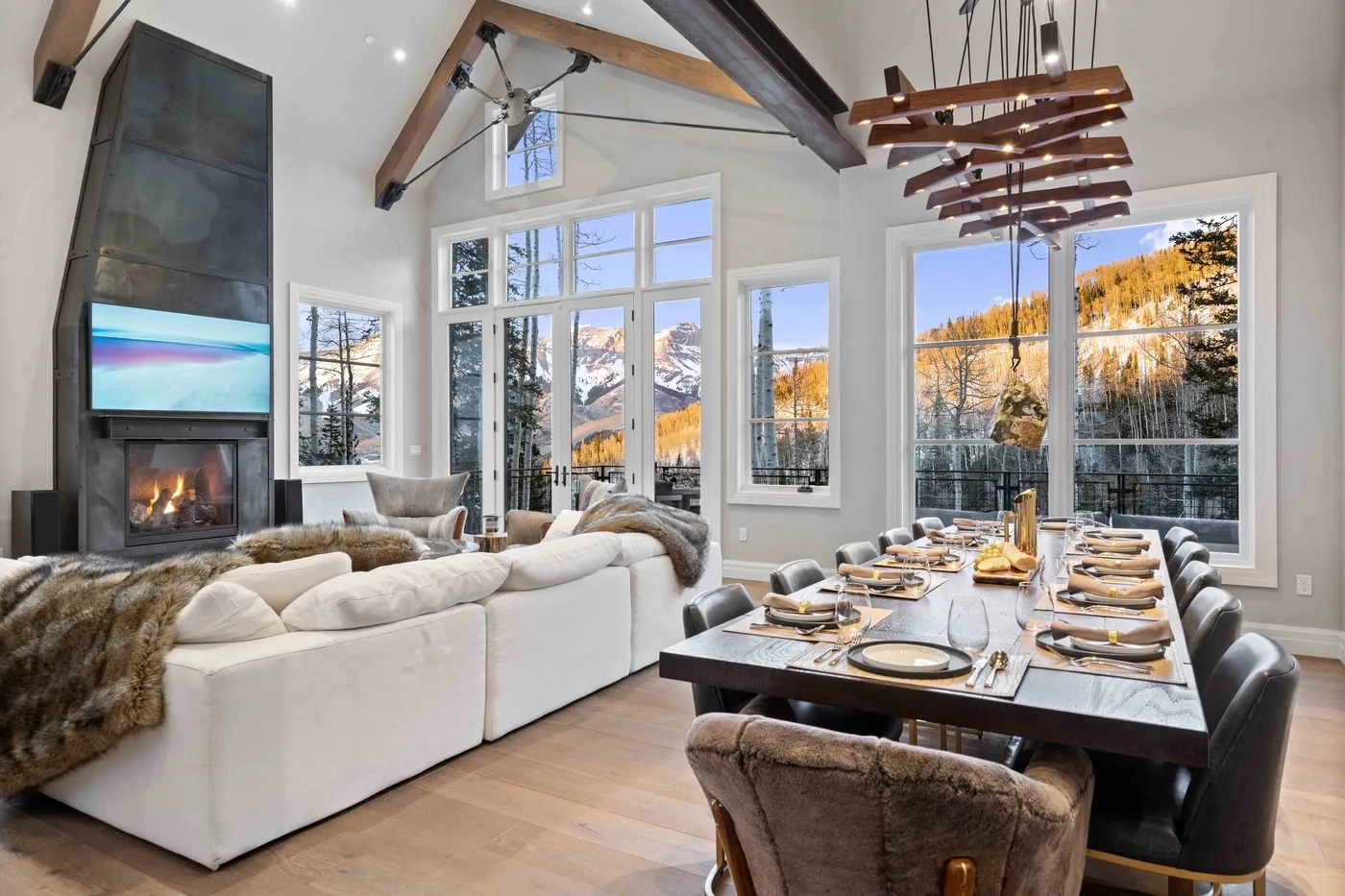 A bright open living and dining area has large windows overlooking a mountain landscape.