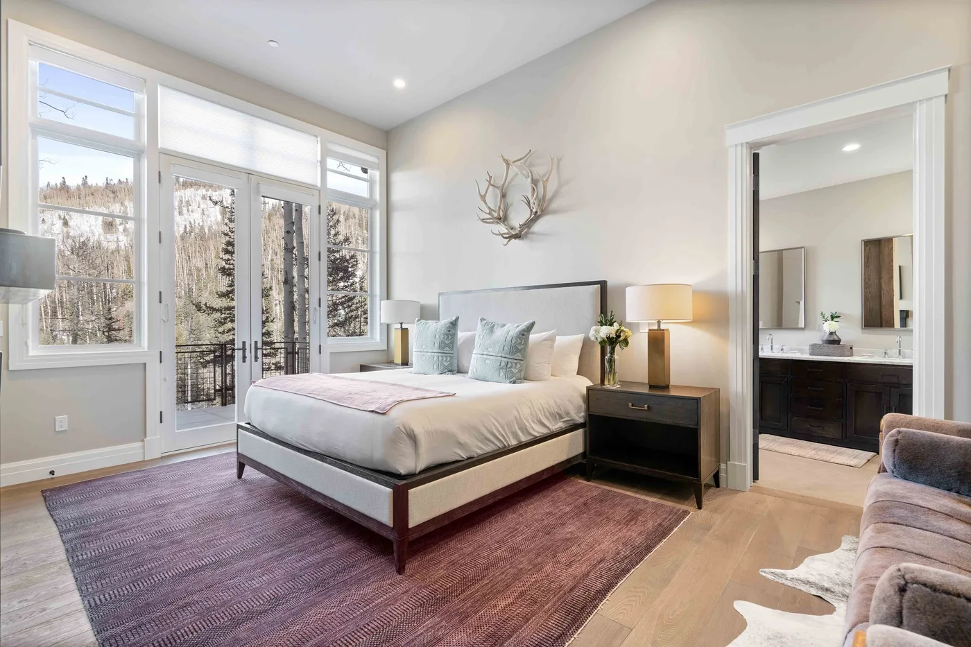 A bright bedroom with a bed, large windows, and an open doorway to a bathroom.