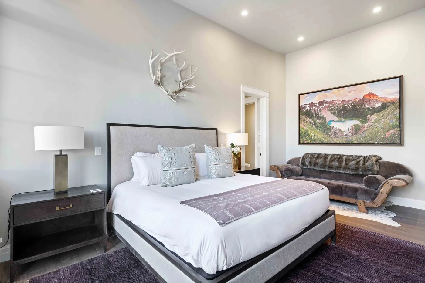 A bedroom with a large bed and a seating area beneath a framed landscape picture.