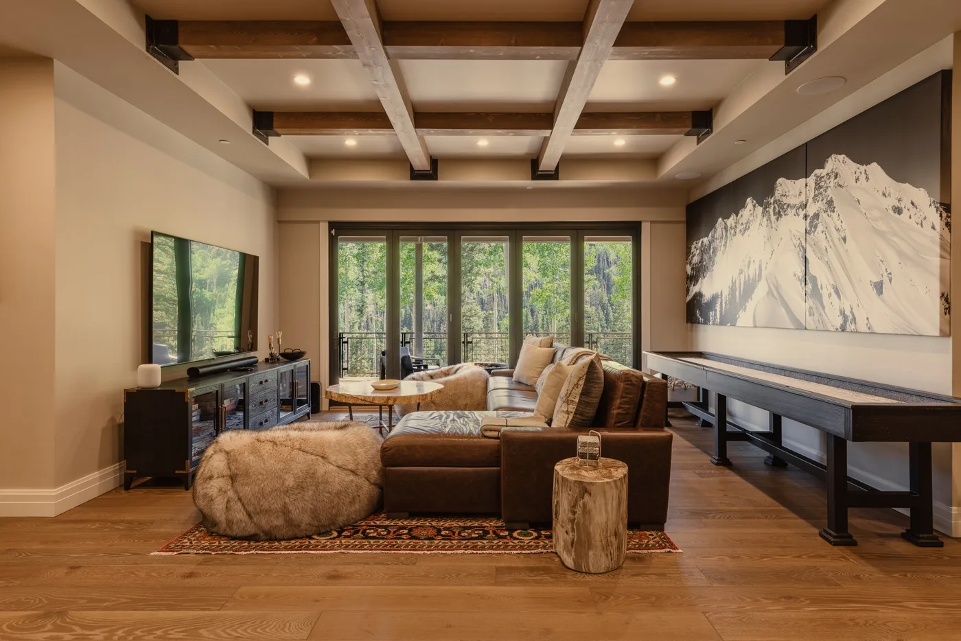 A living room with seating, a television, and large windows overlooking greenery.
