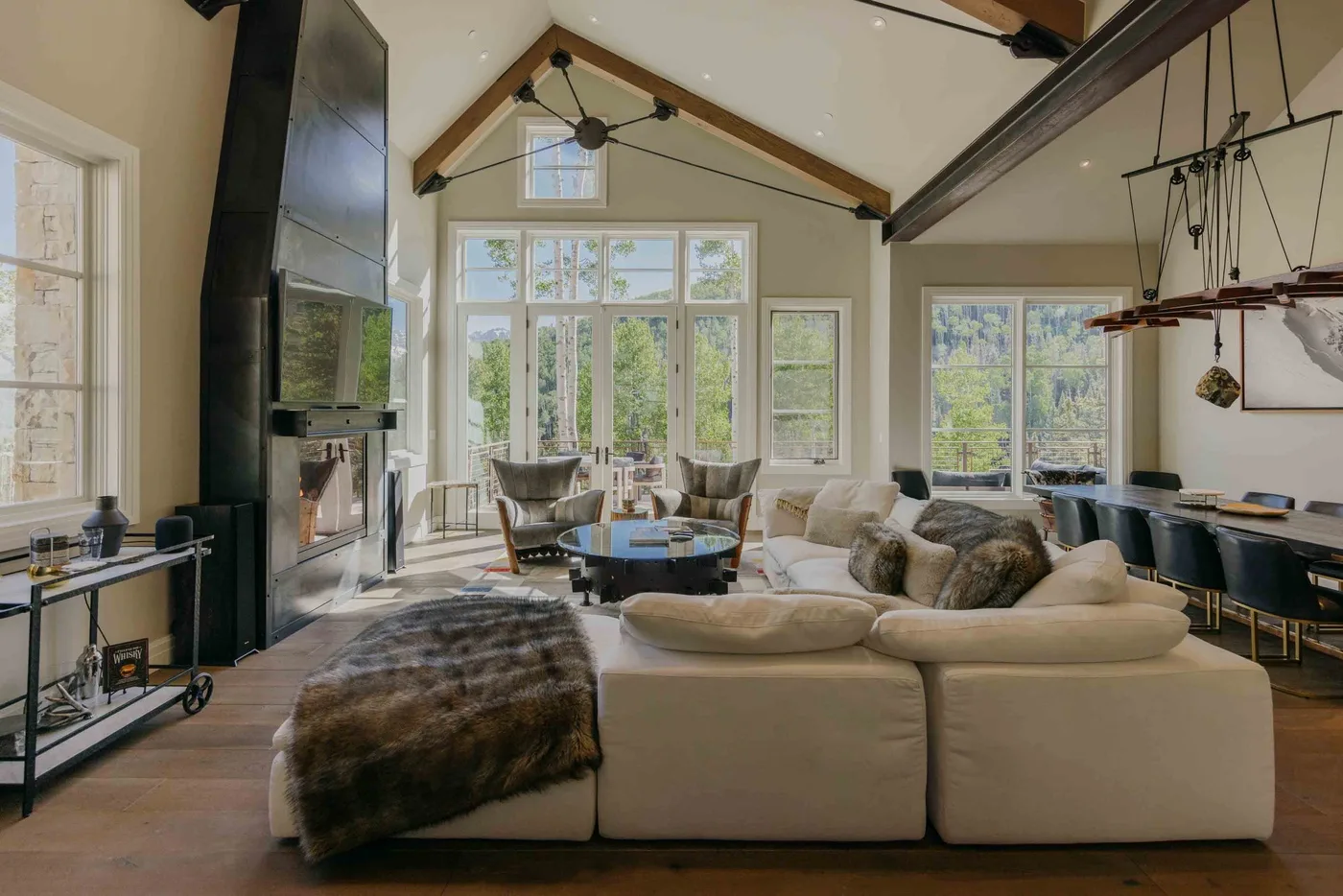 A bright living room with large windows and a seating area around a coffee table.