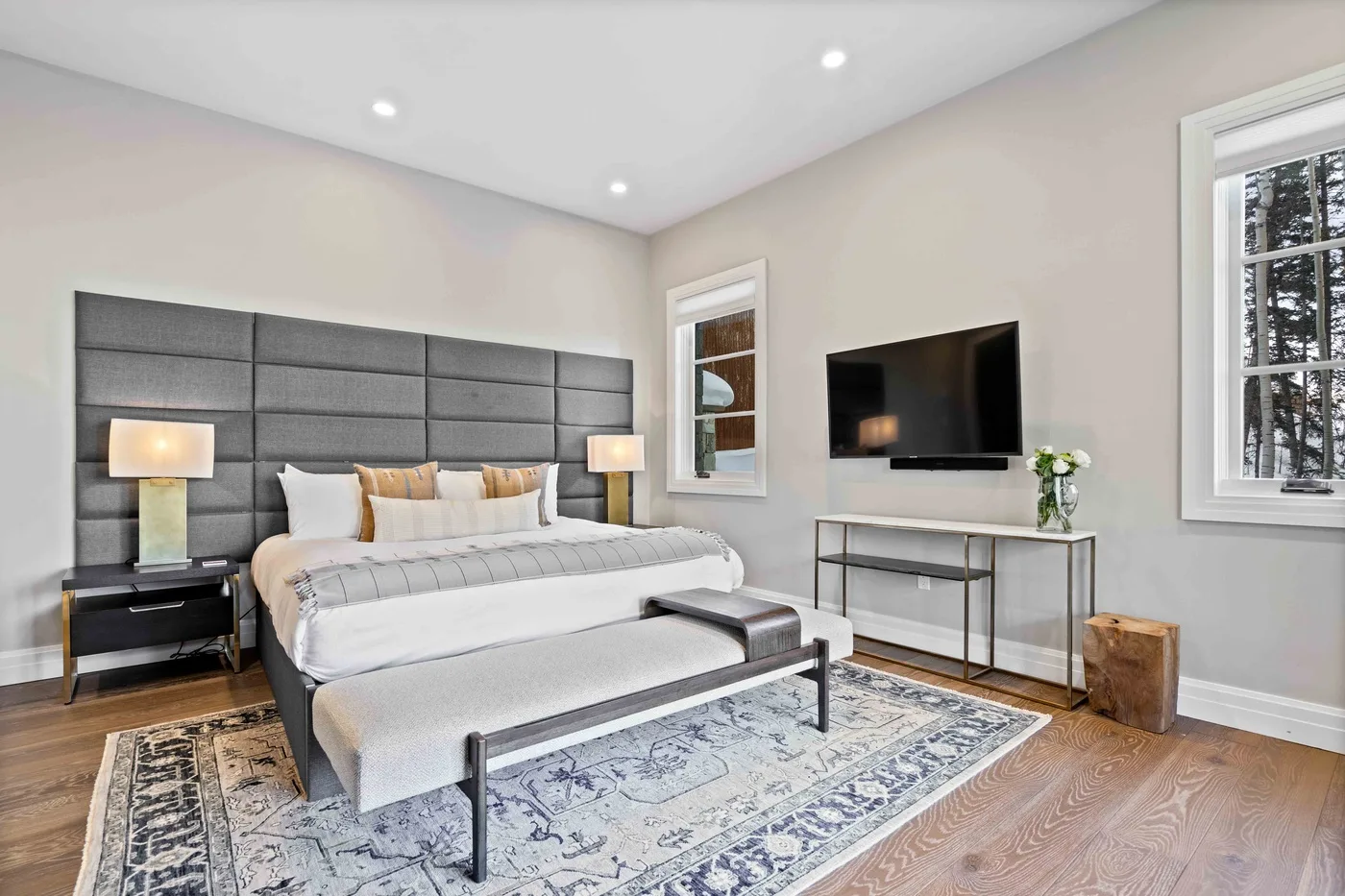 A bright bedroom features a bed, bedside tables, and a wall-mounted television.