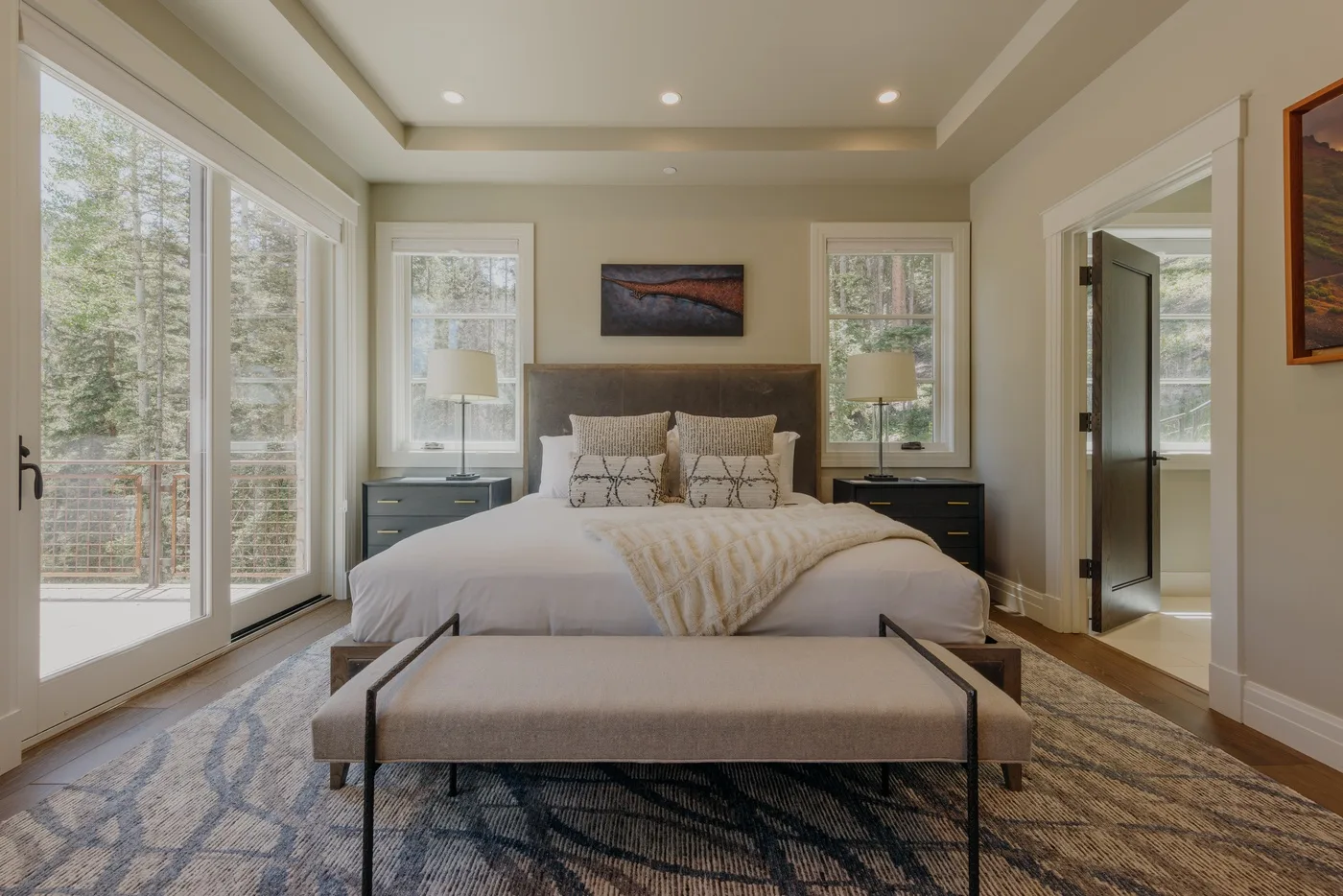 A bedroom with a bed, bedside tables, and tall windows.