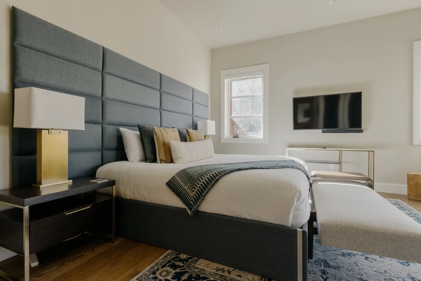 A bedroom with a neatly made bed, a wall-mounted television, and a window.