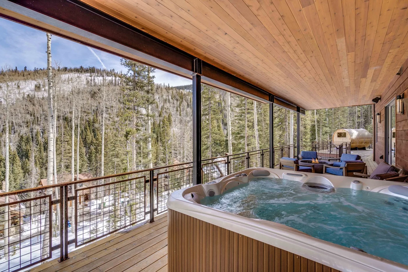 A covered outdoor deck features a bubbling hot tub overlooking a snowy forest.