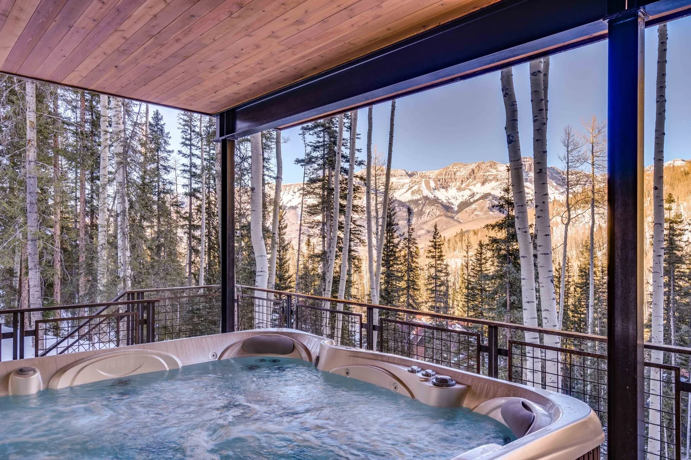 An outdoor hot tub sits on a covered deck overlooking a forested mountain landscape.