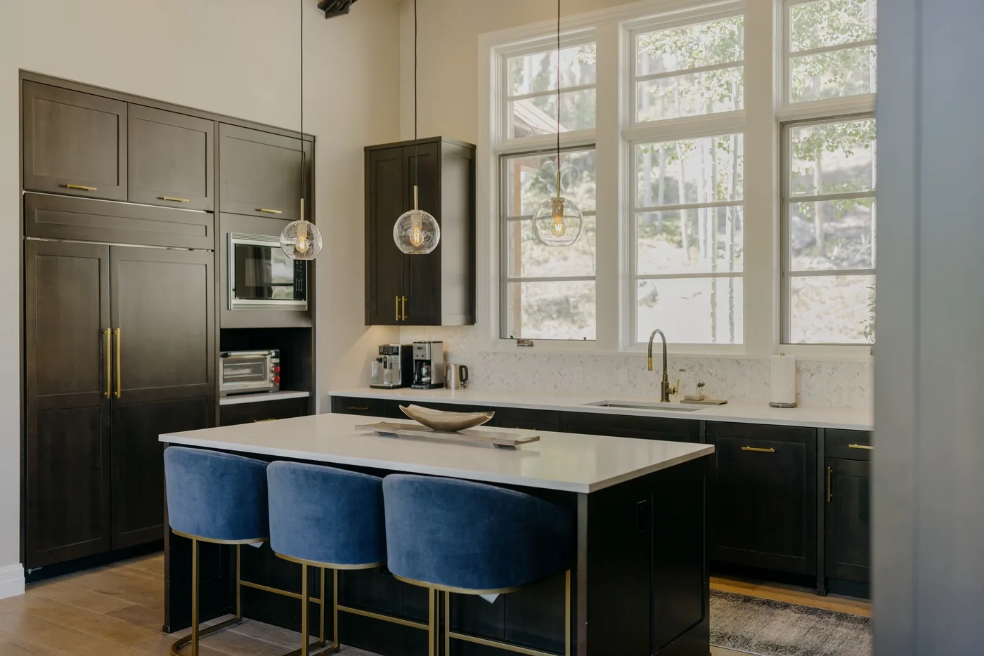 A bright kitchen with dark cabinets, a large island, and tall windows.