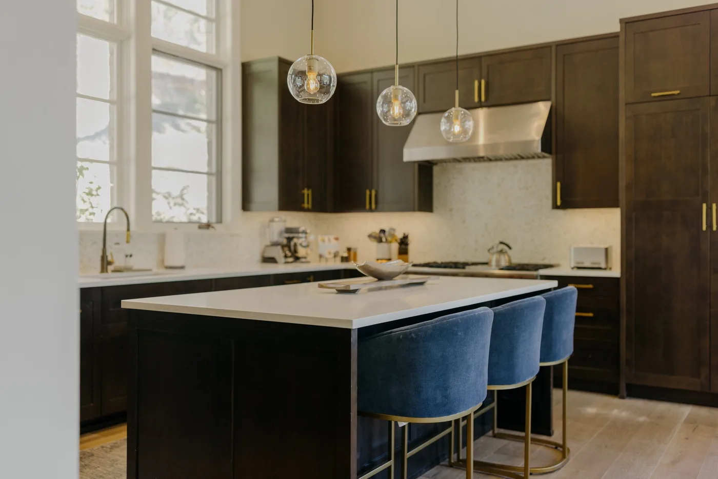 A modern kitchen with dark cabinets, a central island, and blue seating.