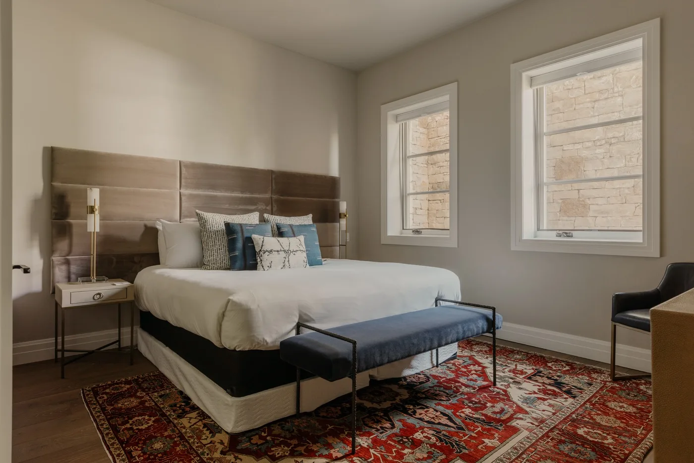A bedroom with a neatly made bed and two tall windows.