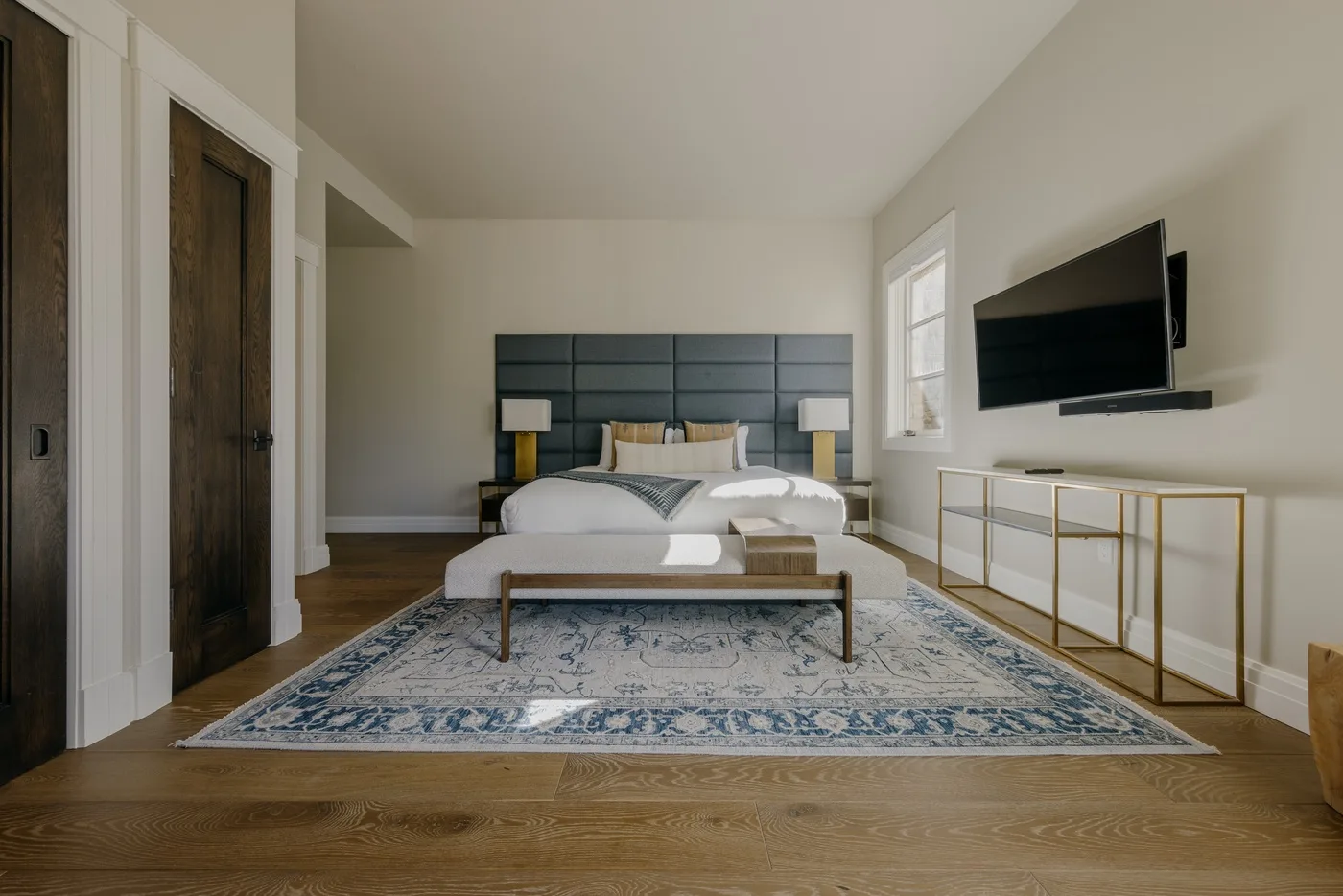 A bedroom with a bed centered on a patterned rug and a wall-mounted television.