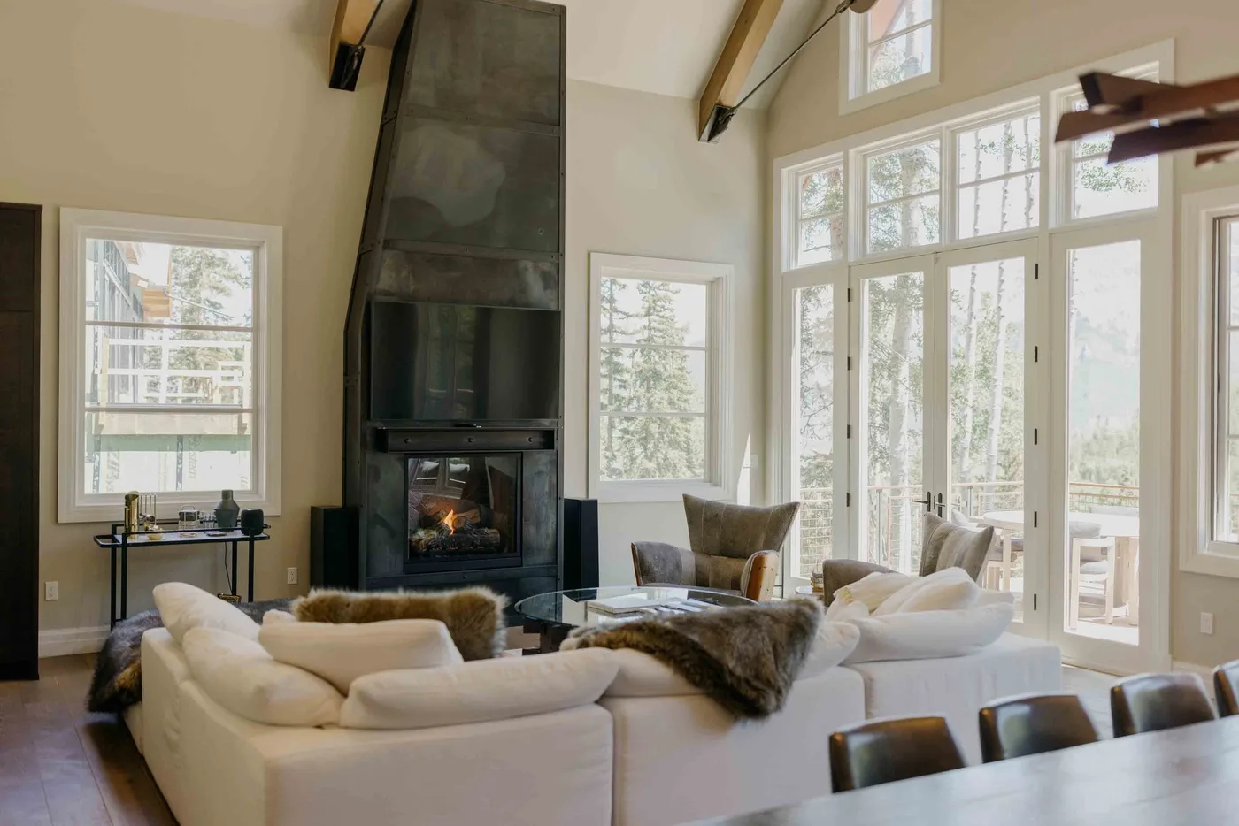 A bright living room with seating arranged around a fireplace and tall windows.