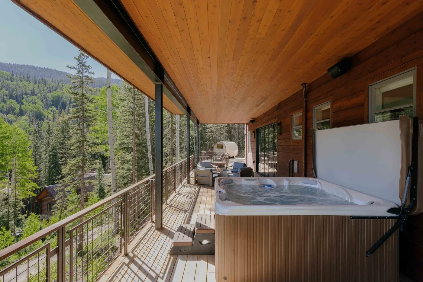 A covered wooden deck with a hot tub overlooks a forested mountain slope.
