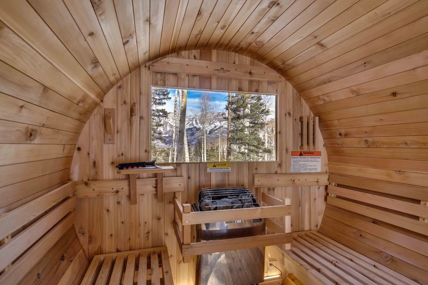 A wood-paneled sauna with tiered seating and a heater beneath a window.