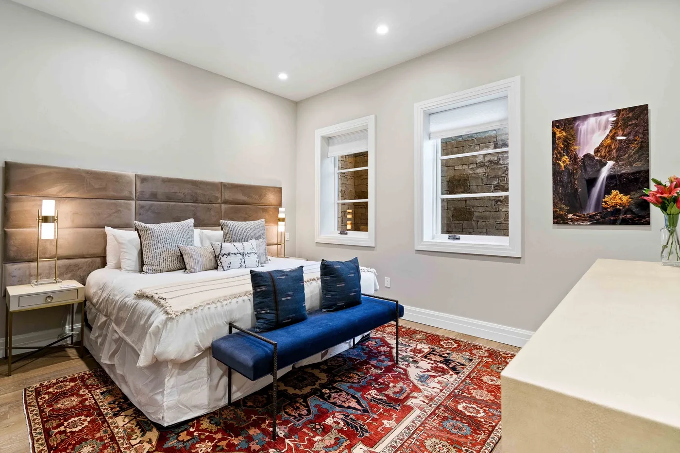 A bedroom with a bed, blue bench, and patterned rug.