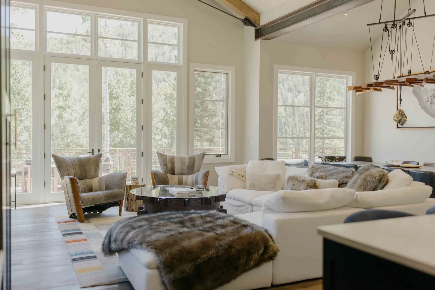 A bright living room with large windows and seating arranged around a low table.