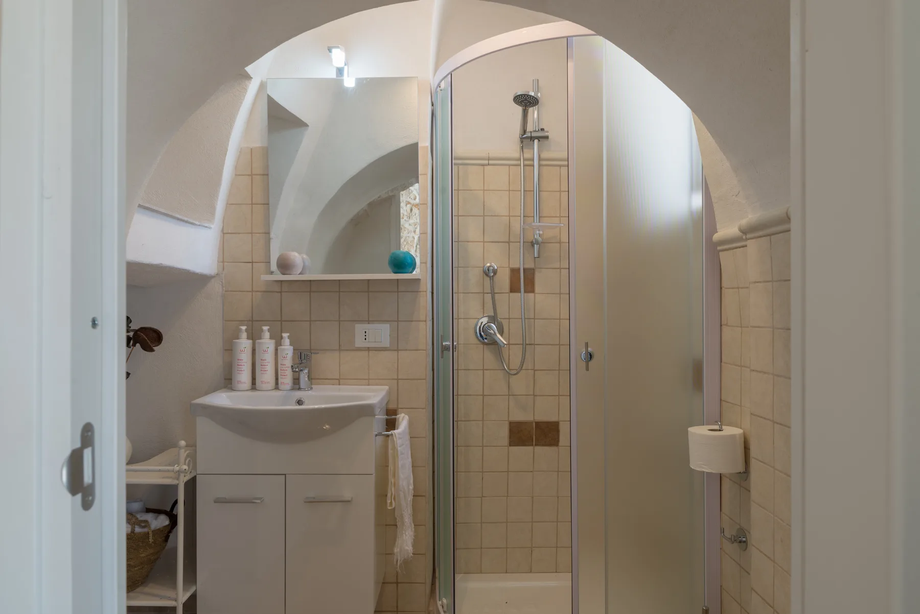 Un baño con lavabo y ducha de vidrio bajo un techo abovedado.