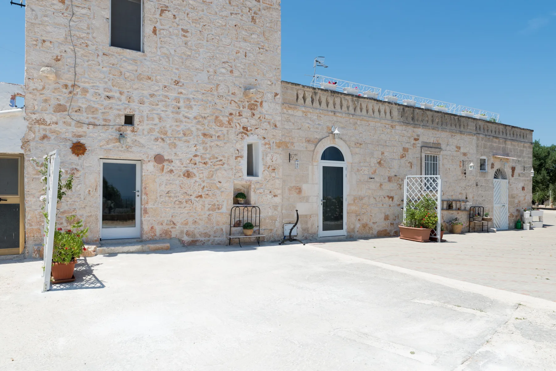 Un edificio de piedra da a un patio soleado con plantas en macetas.