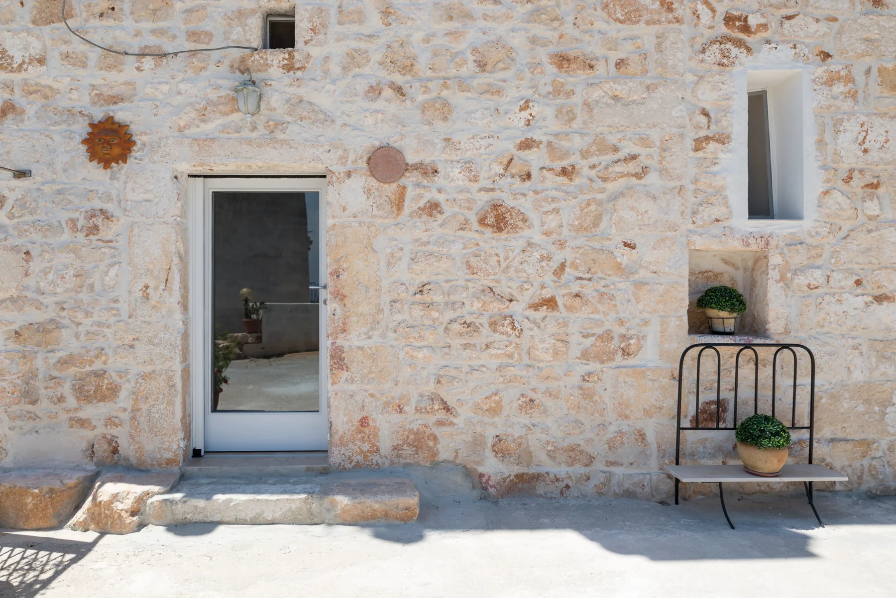 Una pared exterior de piedra clara con una puerta y plantas en macetas sobre un soporte.