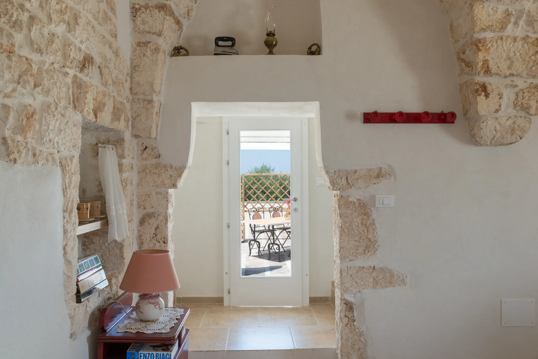 Una habitación con paredes de piedra y una puerta que da a una zona exterior con asientos.