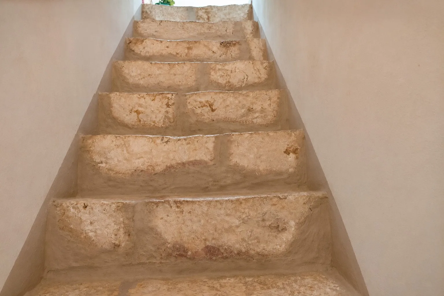 Una estrecha escalera de piedra sube entre paredes lisas.