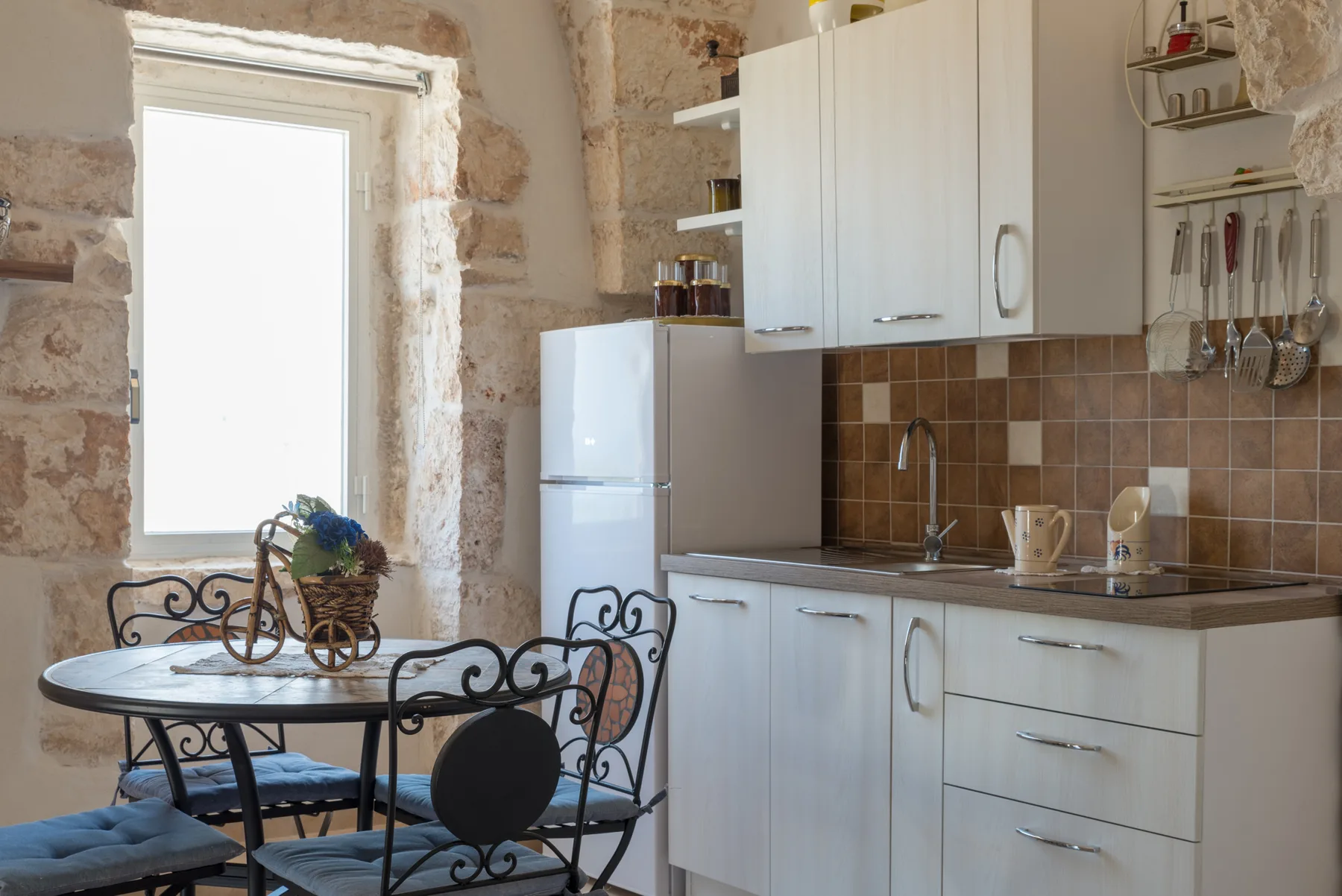 Una cocina compacta con gabinetes blancos, un refrigerador y una pequeña mesa de comedor.