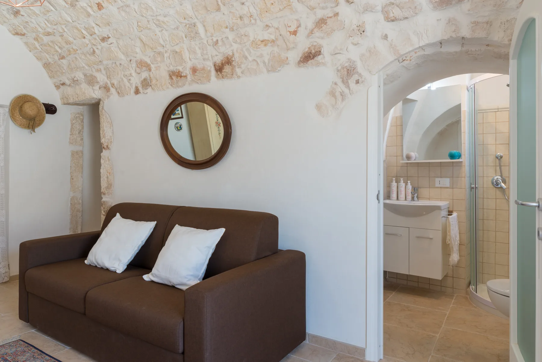 Una zona de estar con un sofá marrón queda junto a la entrada arqueada del baño.