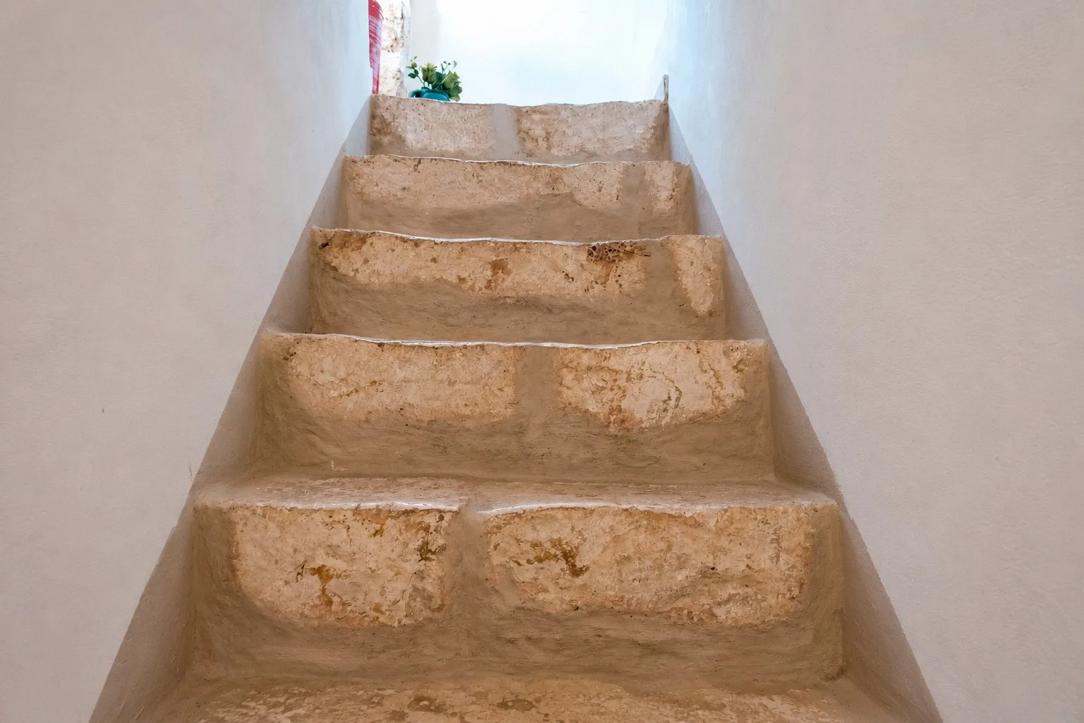 Una escalera estrecha con escalones de piedra desgastados conduce a un rellano iluminado.