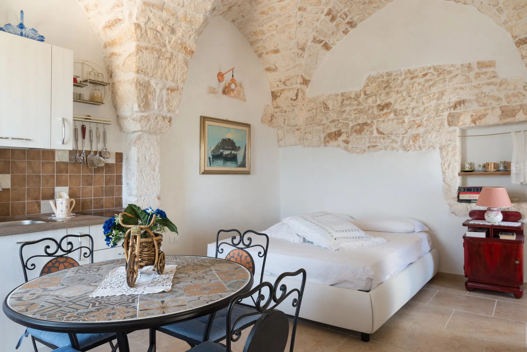 Dormitorio y zona de comedor bajo un arco de piedra, con una cama y una mesa redonda.