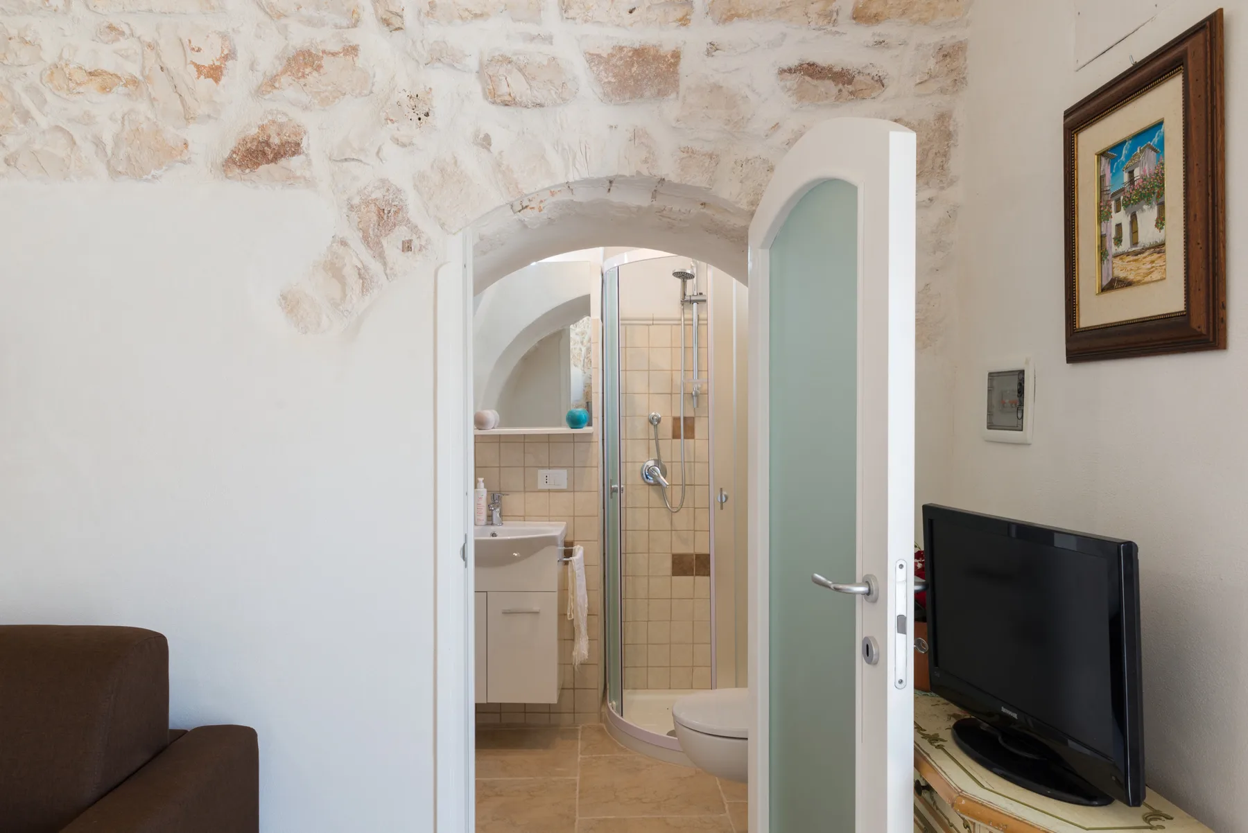 Se ve un baño a través de una puerta abierta, con ducha y lavabo.