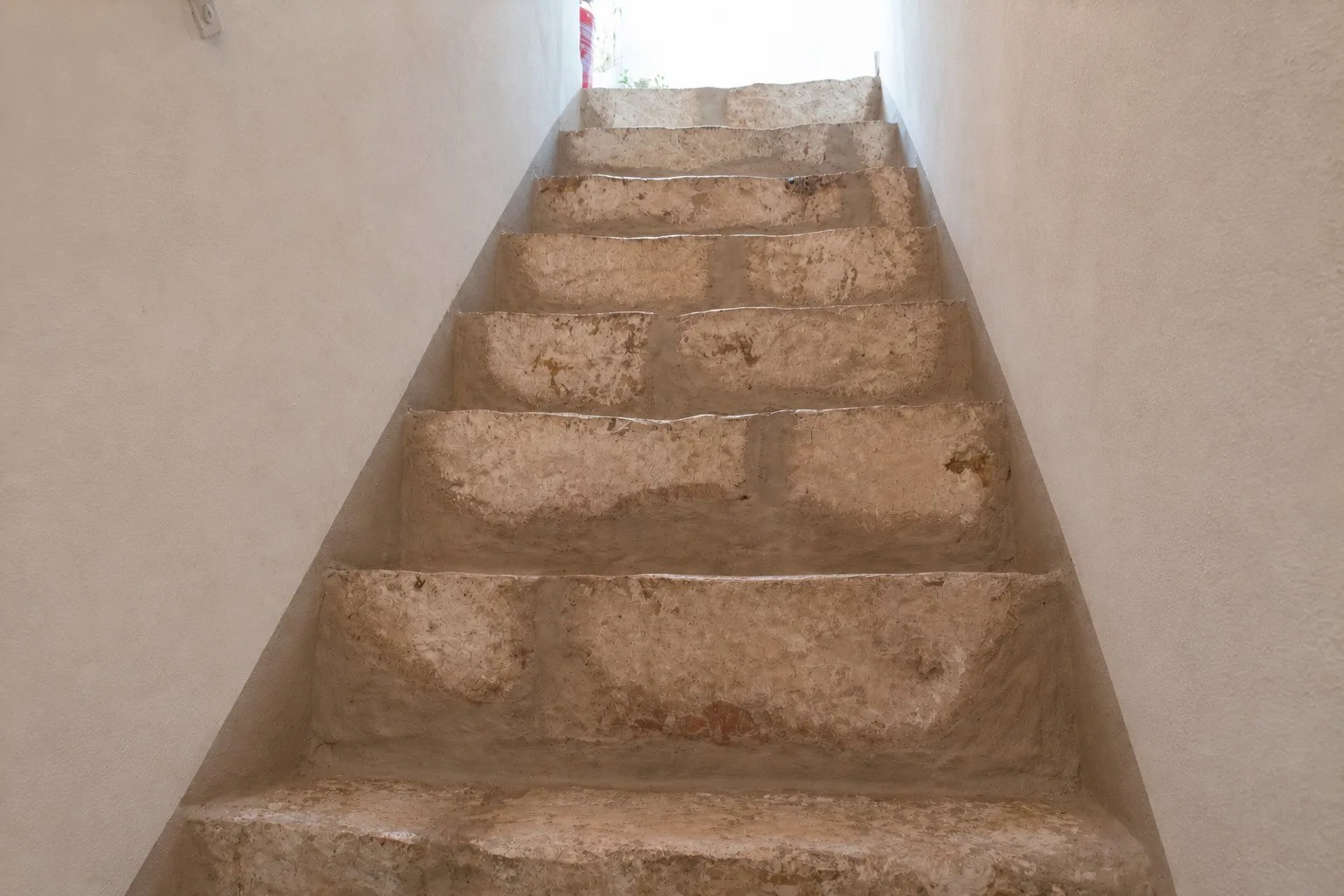 Una escalera estrecha de peldaños de piedra conduce hacia una abertura luminosa.