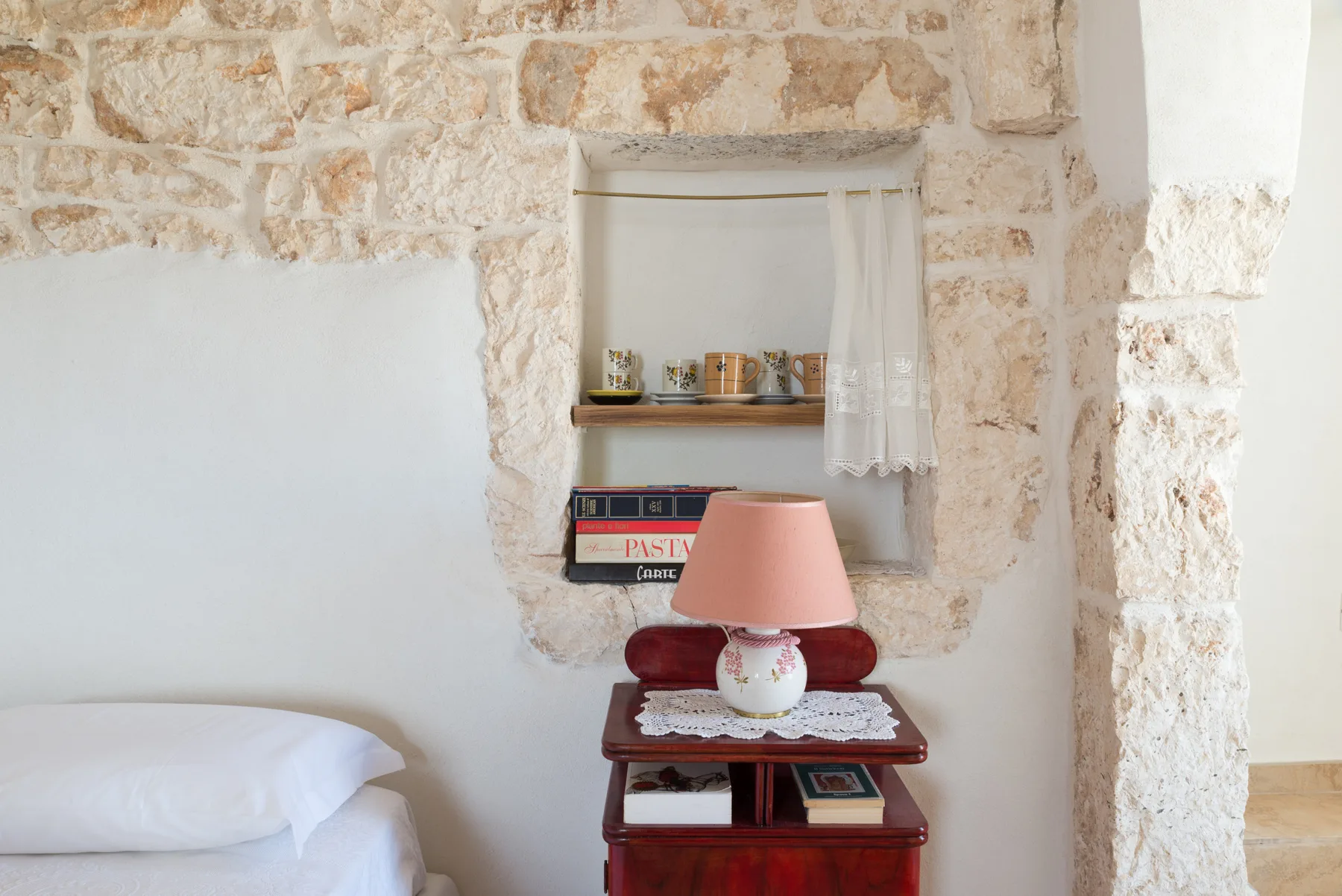 Un rincón de dormitorio con una cama junto a una pequeña mesa de madera y un estante empotrado.