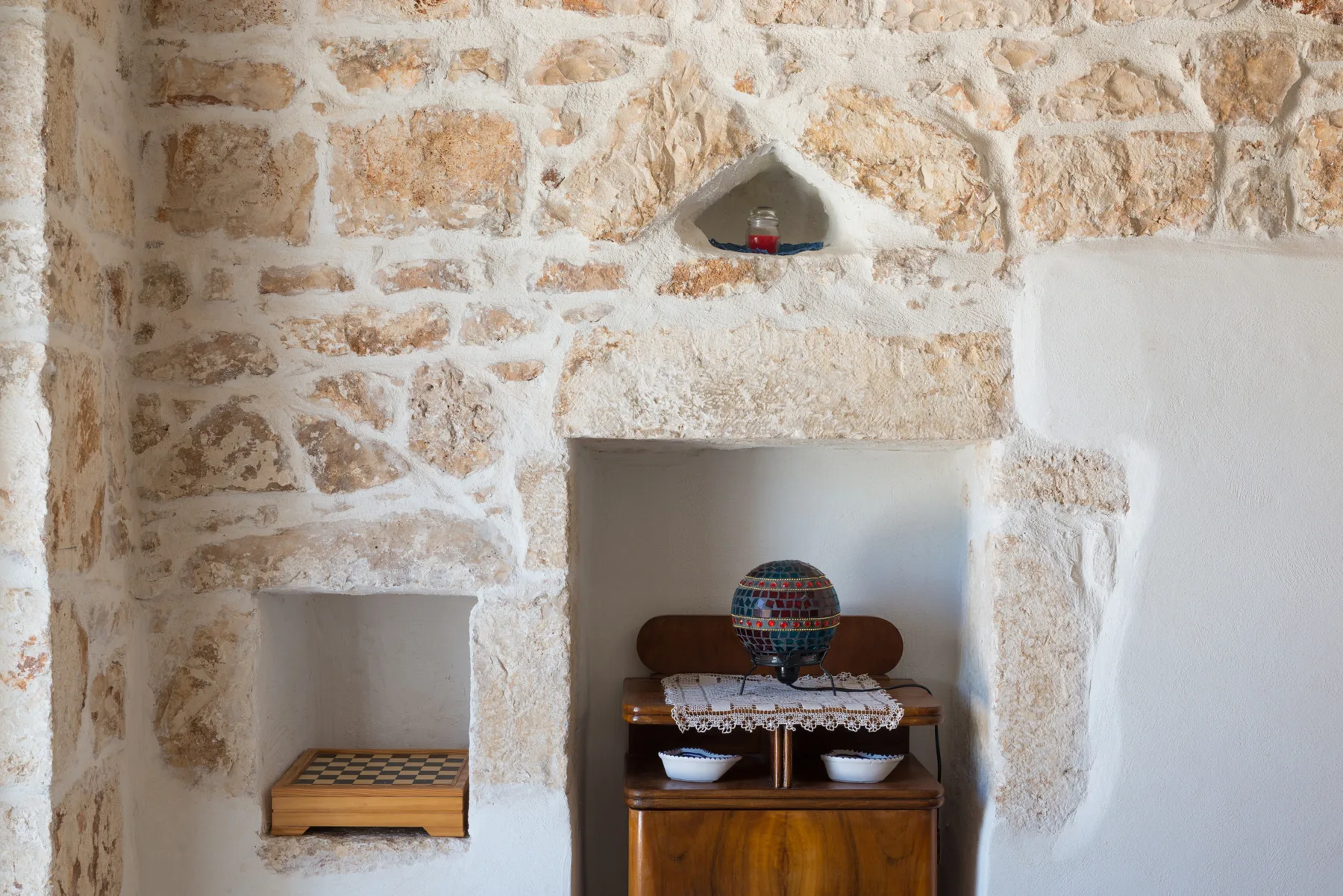 Interior de piedra rústica con un mueble de madera y nichos empotrados en la pared.