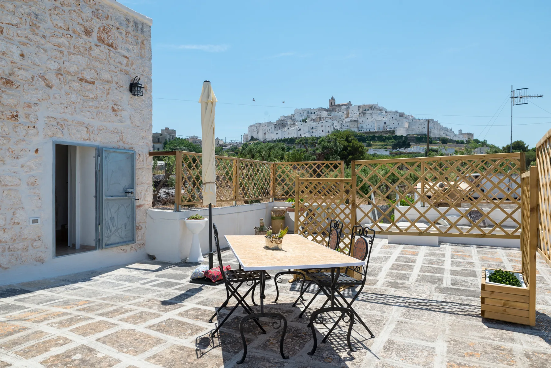 Una terraza de piedra soleada con asientos al aire libre y vistas a un pueblo en una colina.