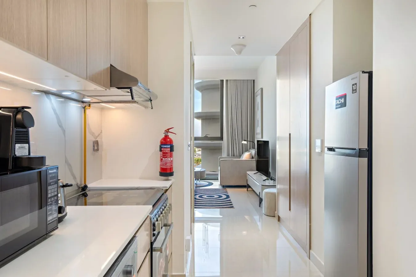 A narrow kitchen opens onto a living area with a television and seating.