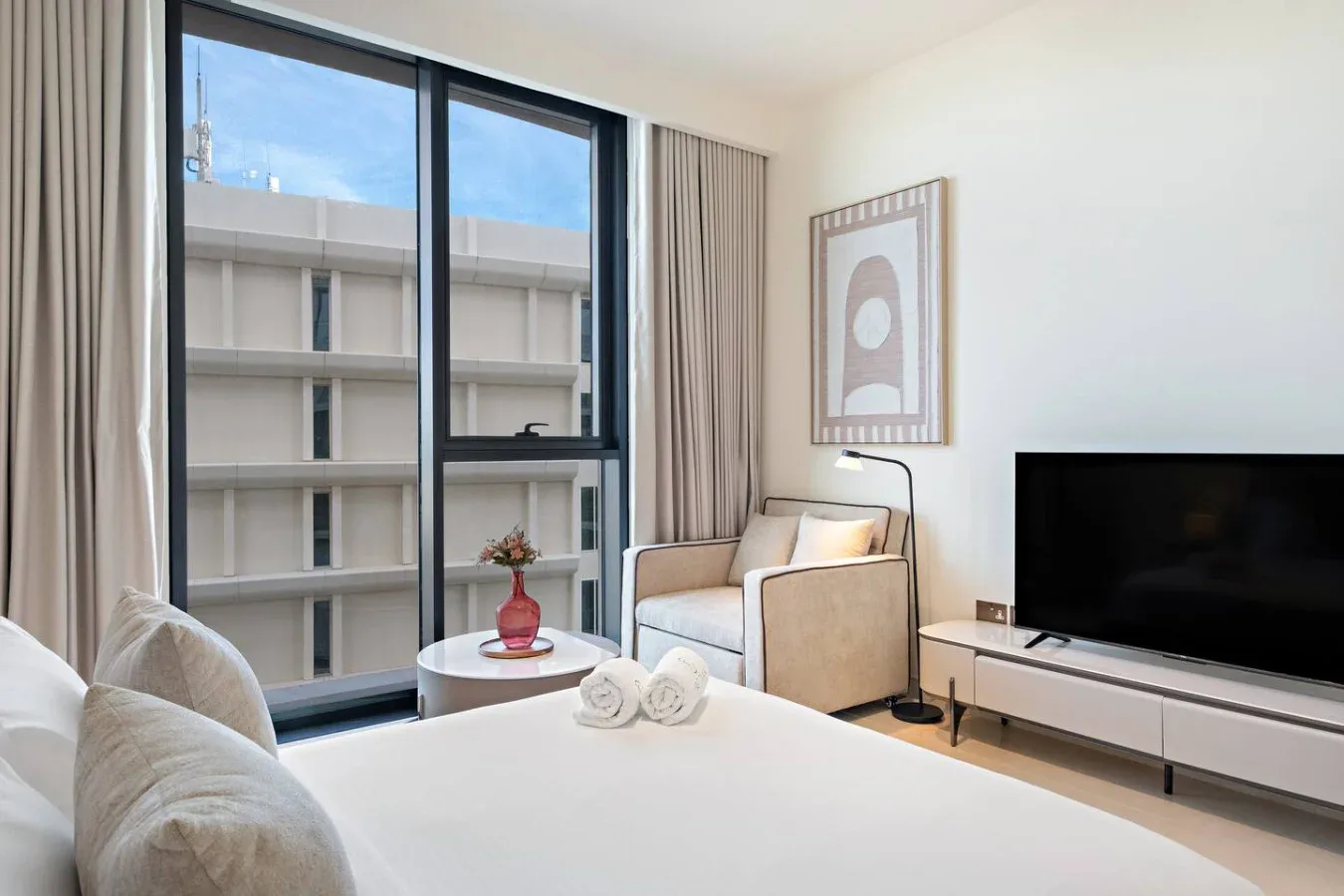 A bright bedroom with a bed, seating area, and large windows.