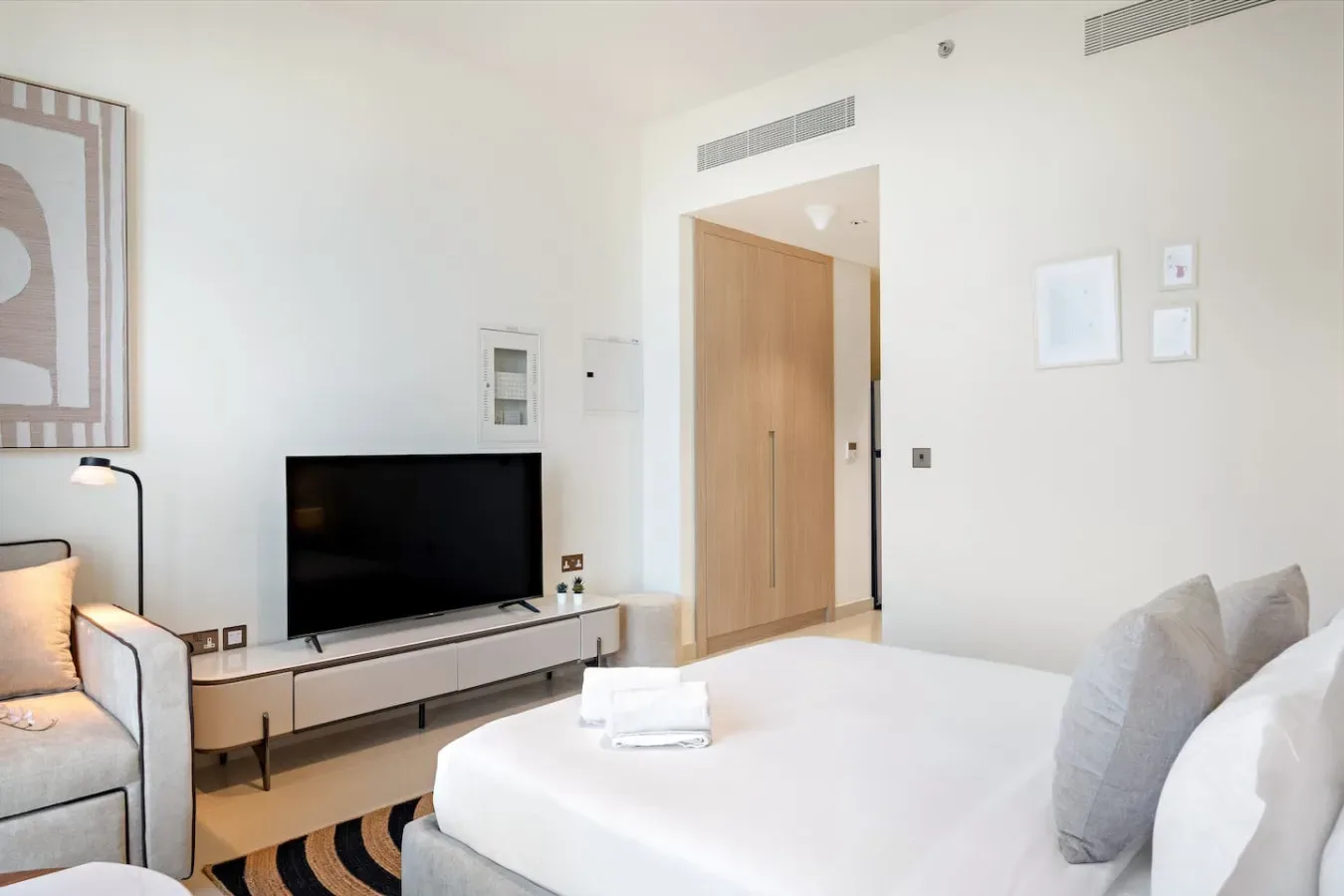 A bright bedroom with a large bed, television, and light-colored furnishings.