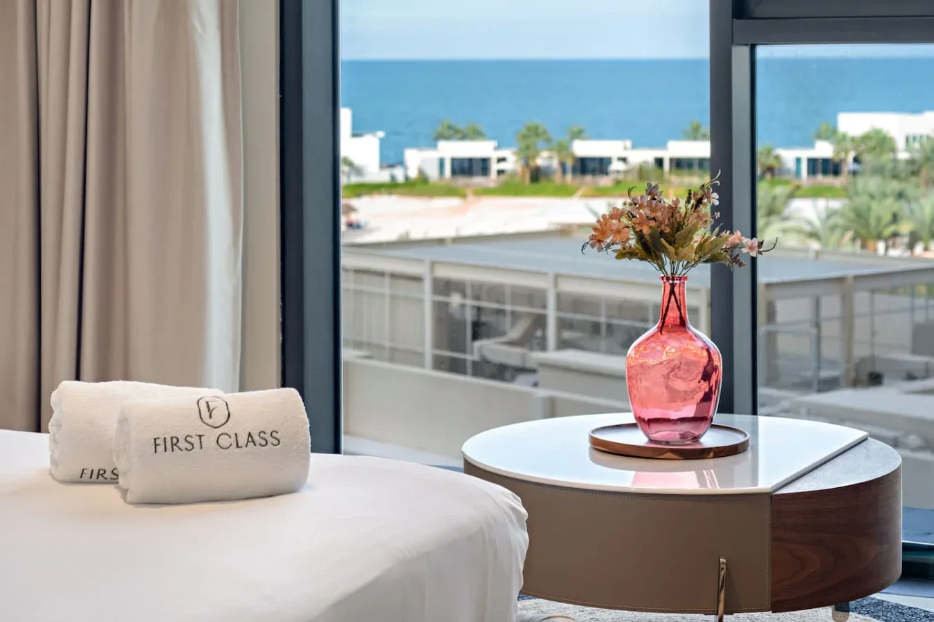 A bedroom seating area with a pink vase beside a large window overlooking the sea.
