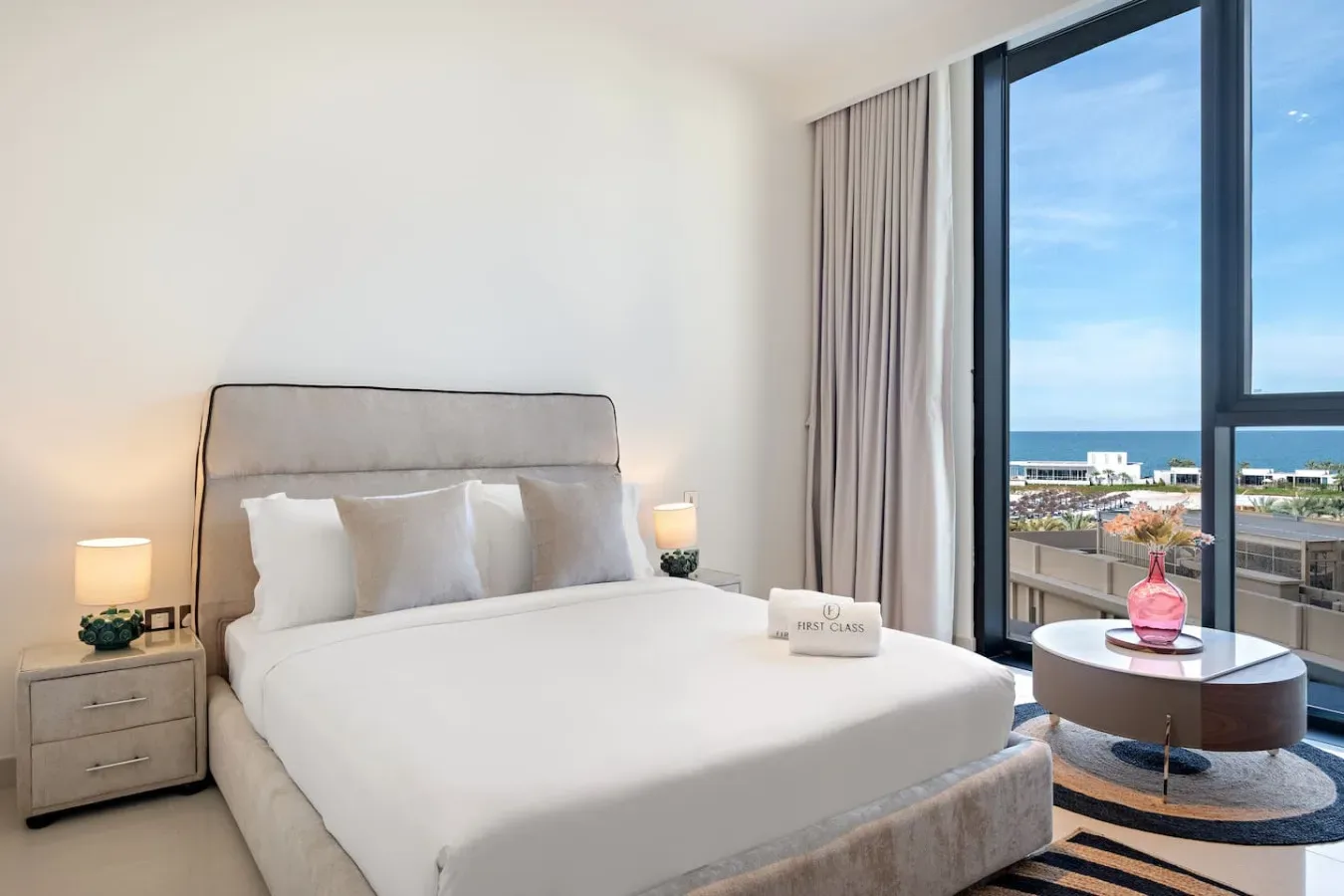 A bedroom with a neatly made bed beside a large window overlooking the sea.