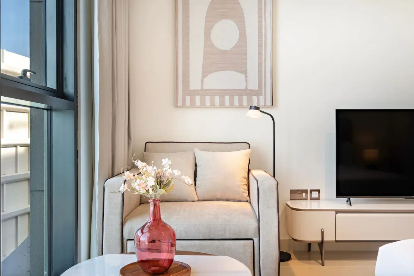 A bright sitting area with a cushioned armchair, side lamp, and television.