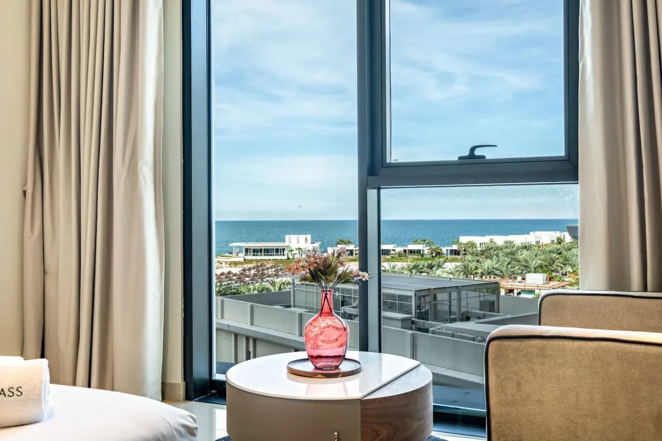 A sitting area by a large window overlooks the ocean and nearby buildings.