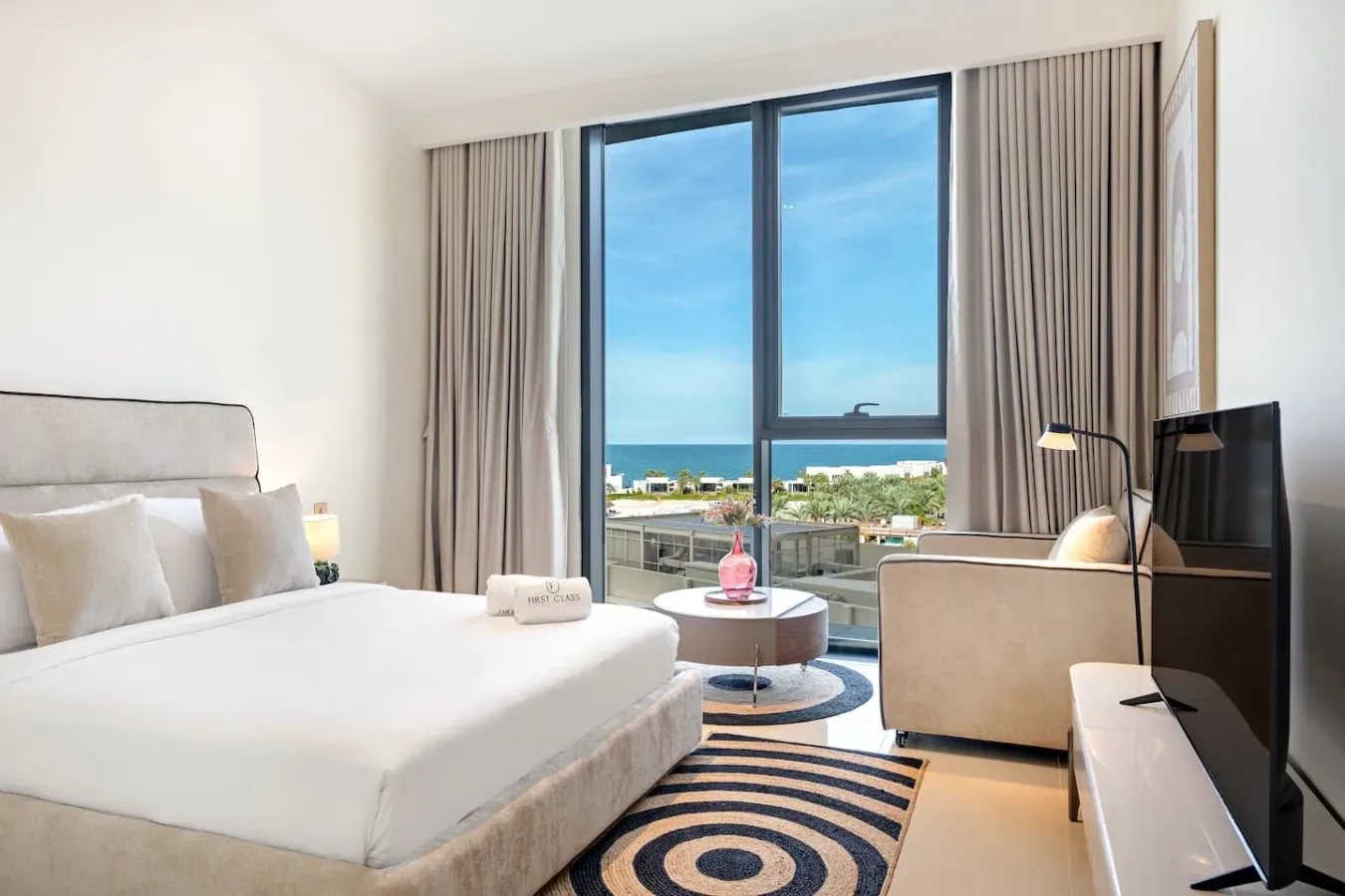 A bright bedroom with a large bed and ocean views through the window.