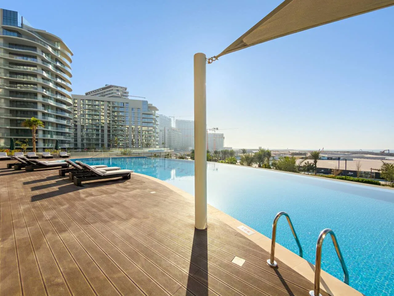 A rooftop pool overlooks nearby high-rise buildings, with loungers on the wooden deck.